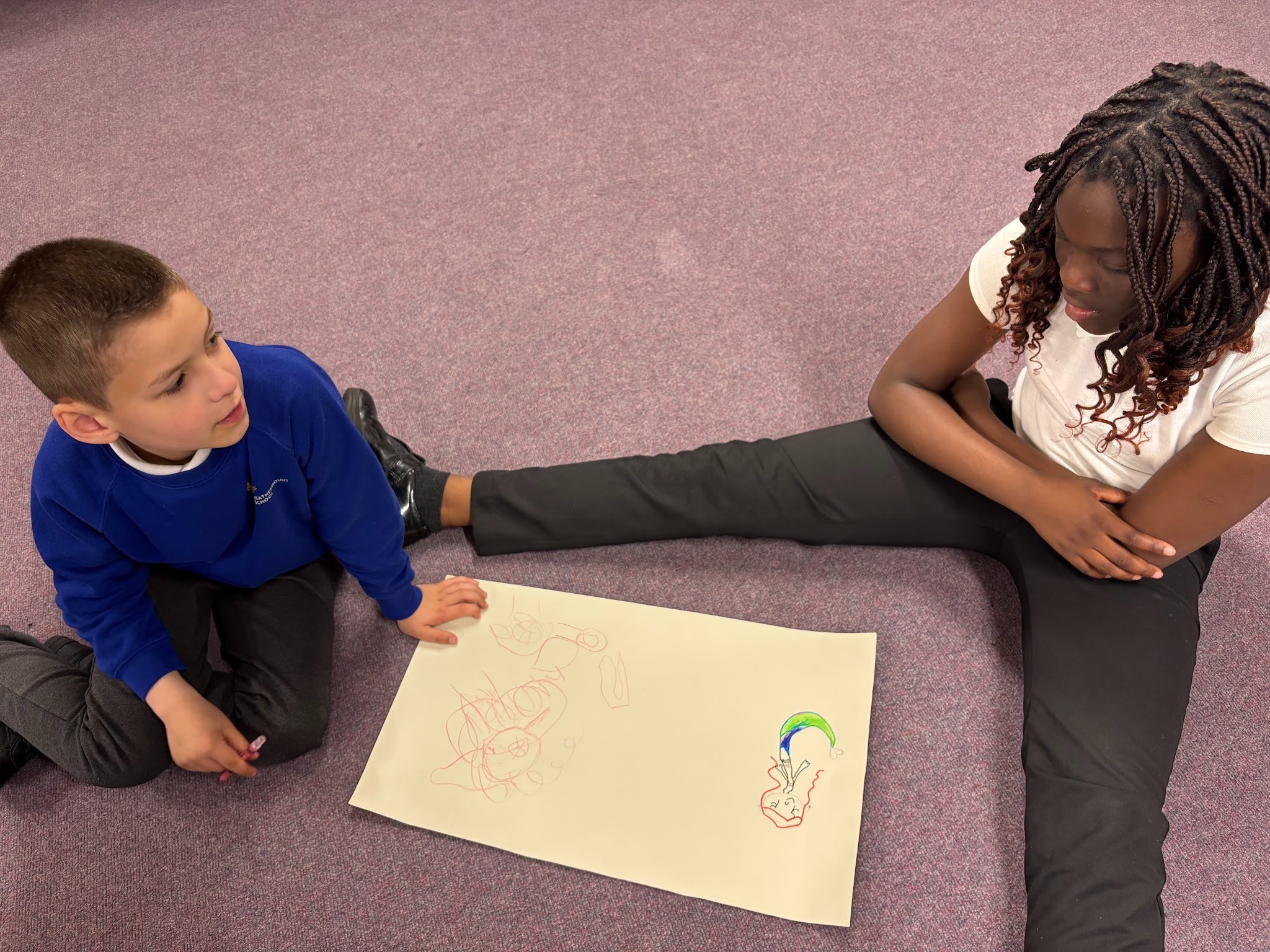 A boy and a girl from Oak class sitting on the floor with their character drawing