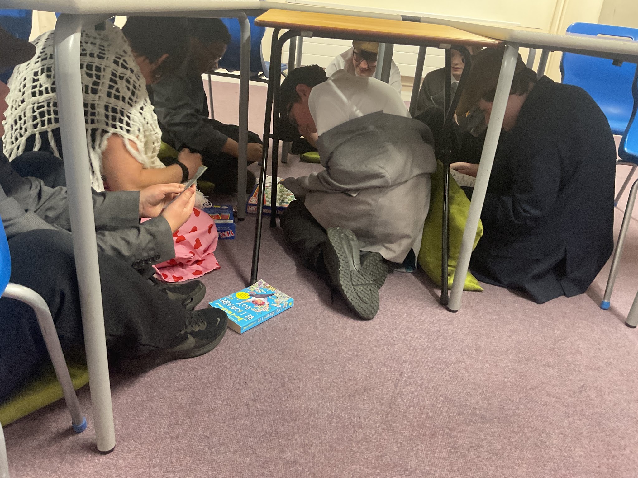 Students acting as a evacuees and pretending to take shelter under a table