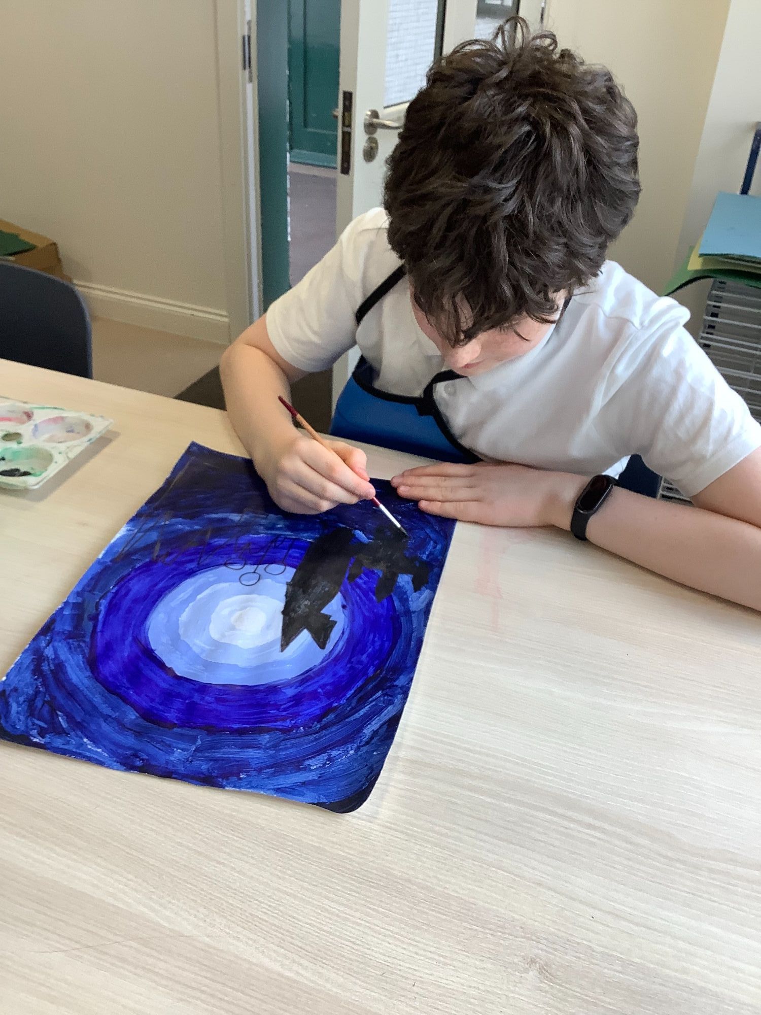 Student painting a silhouette on a blue background
