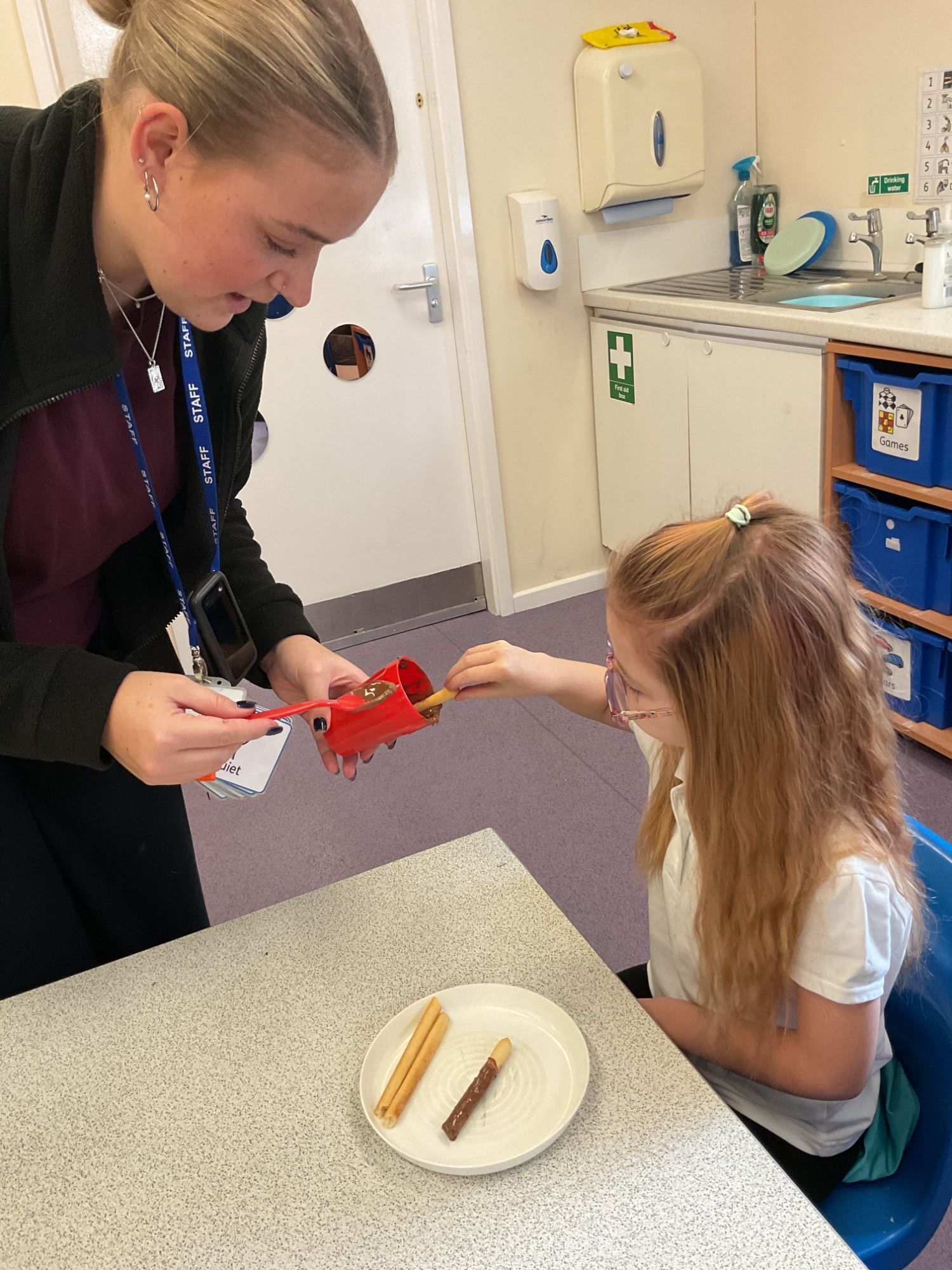 Girl dipping bread stick in chocolate with help from TA