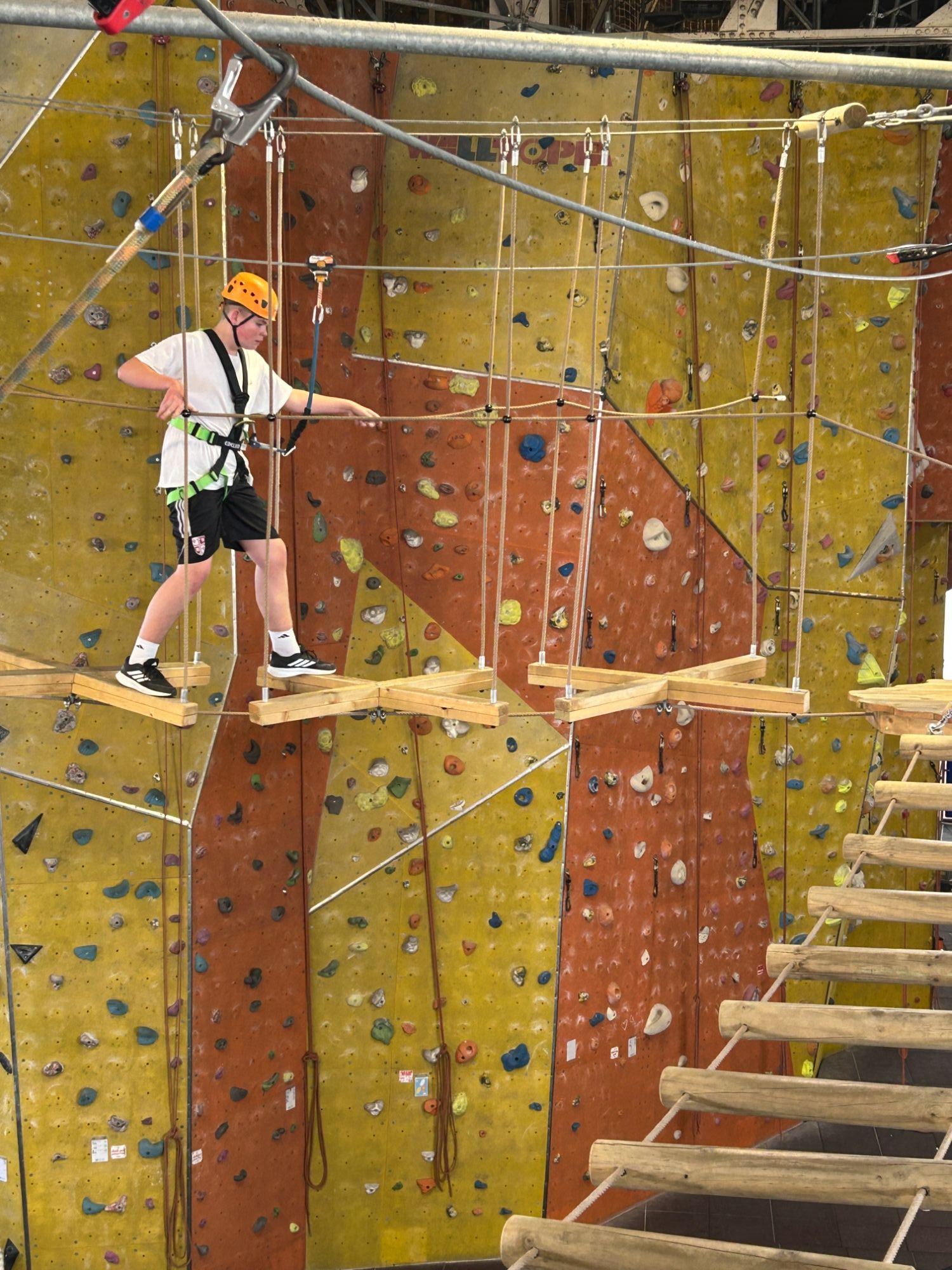 Student with a helmet and harness walking over the high ropes