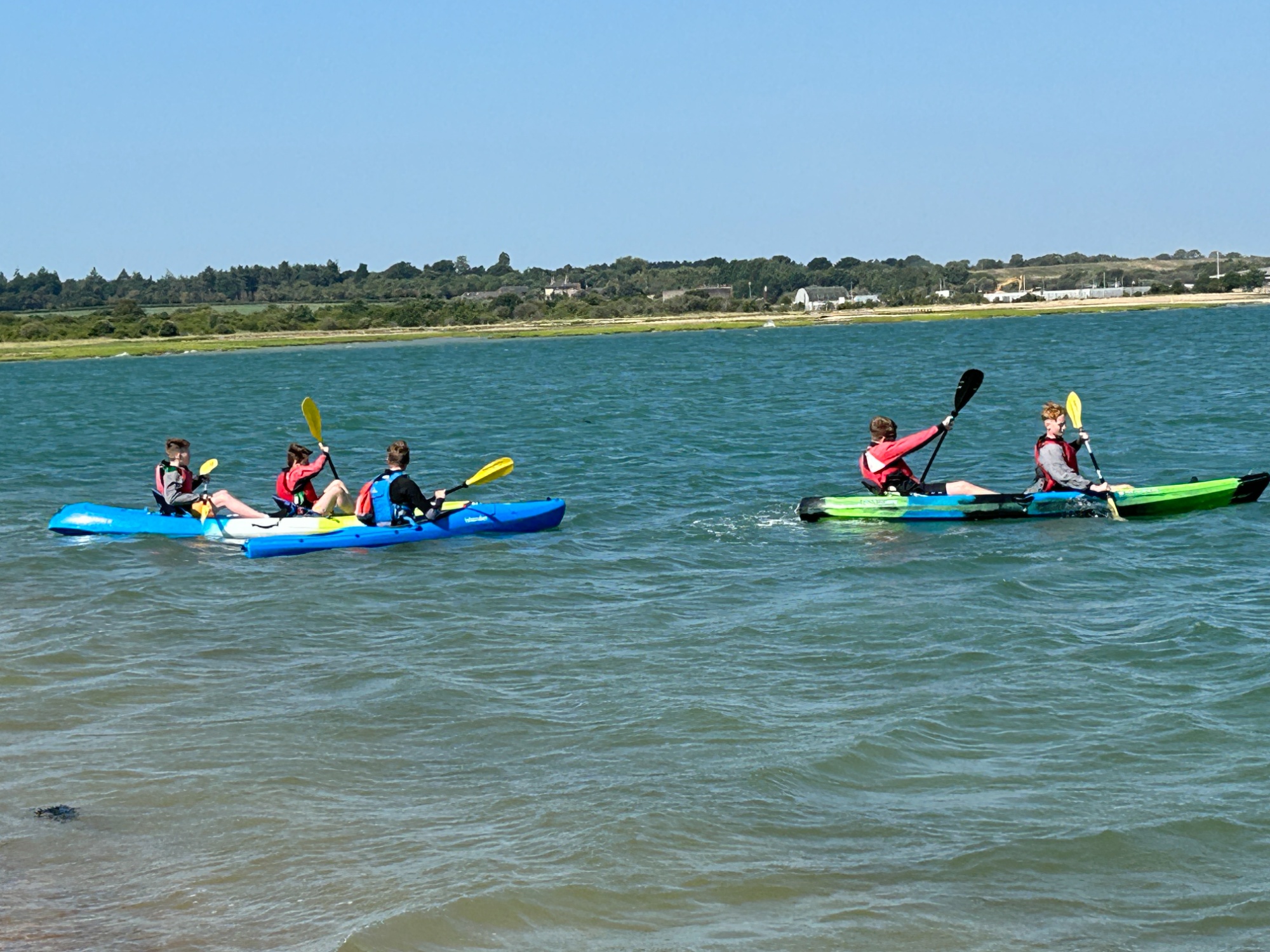 Students paddling kayaks in pairs on the water.