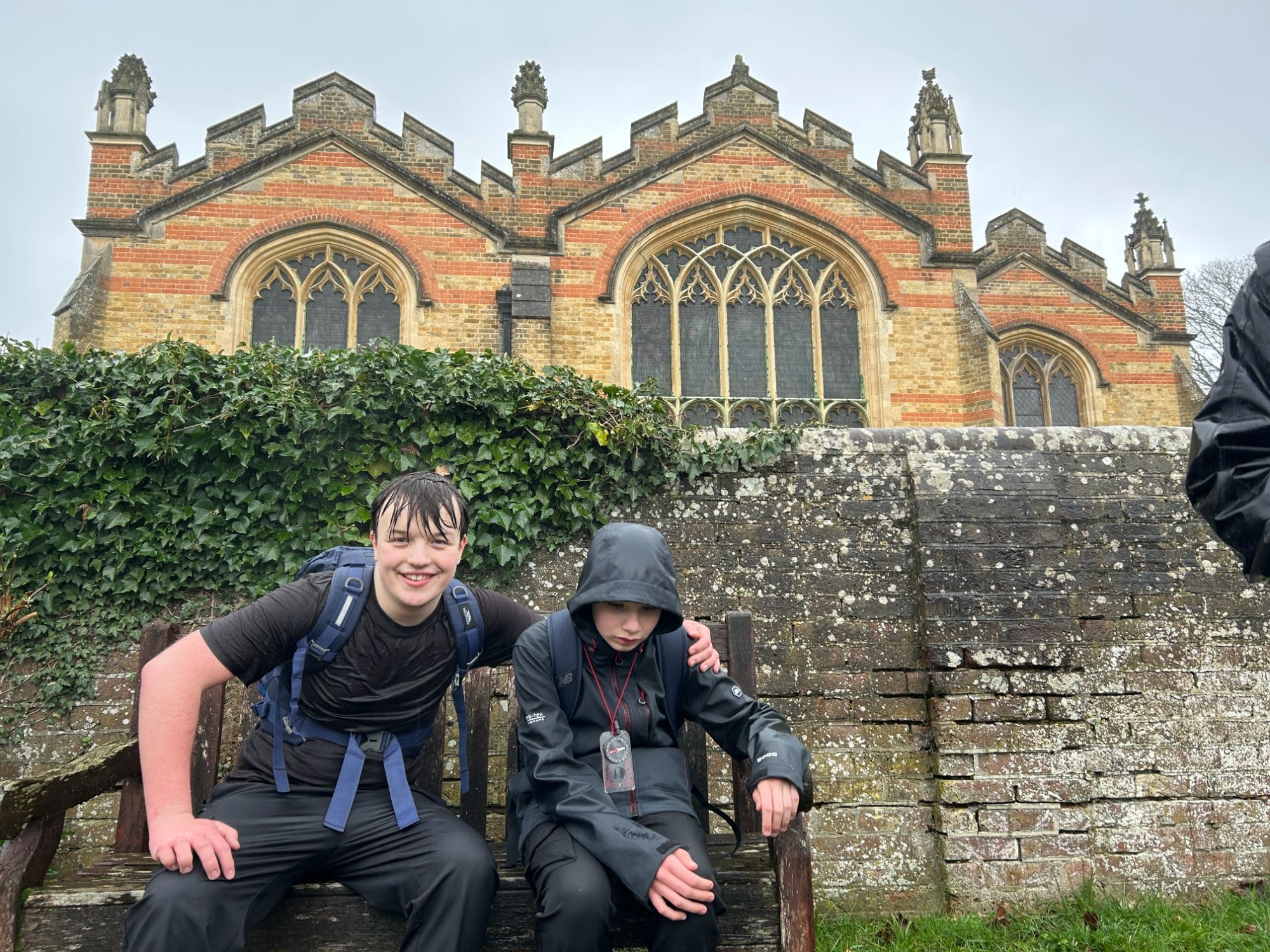 Two students on a bench in the rain one with his arm around the other