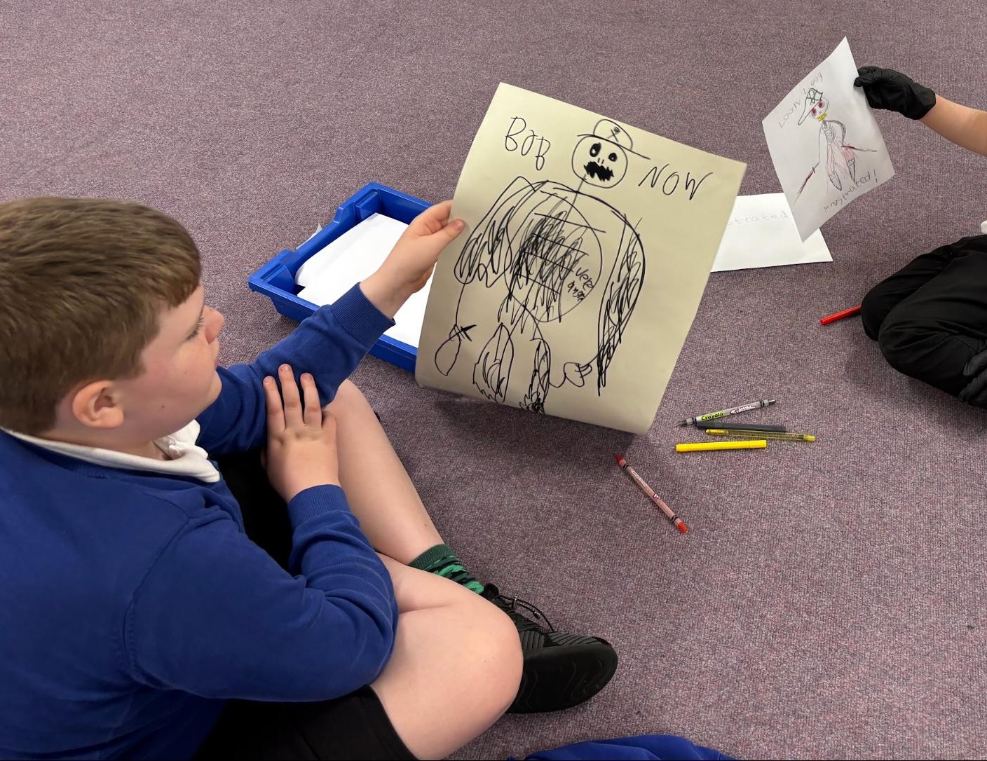 Boy from Oak class holding up his drawing of a character