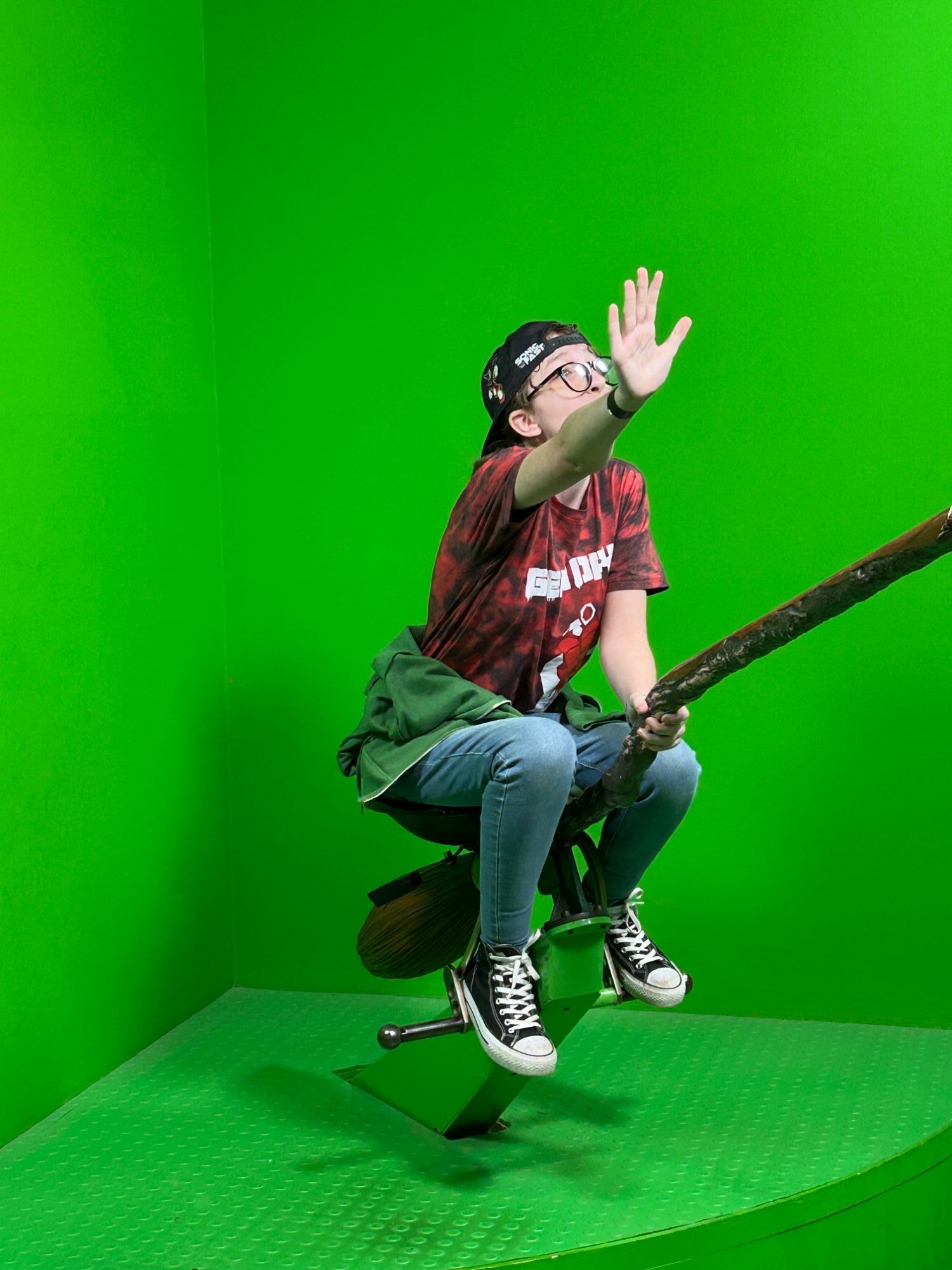 Student riding a broom stick in front of a green screen