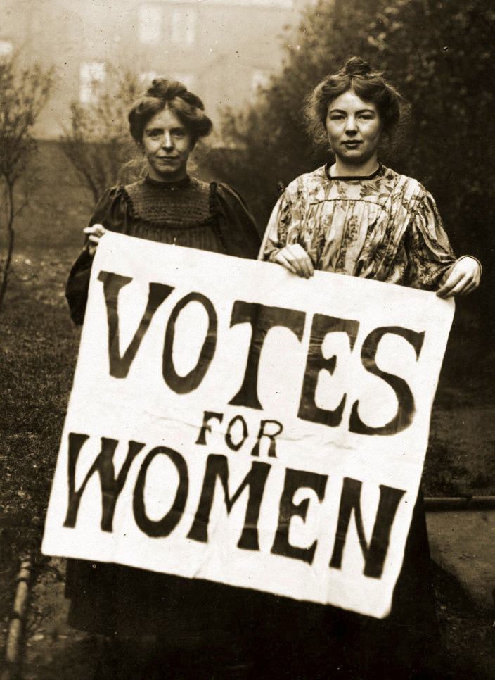 Suffragettes holding  a votes for women sign