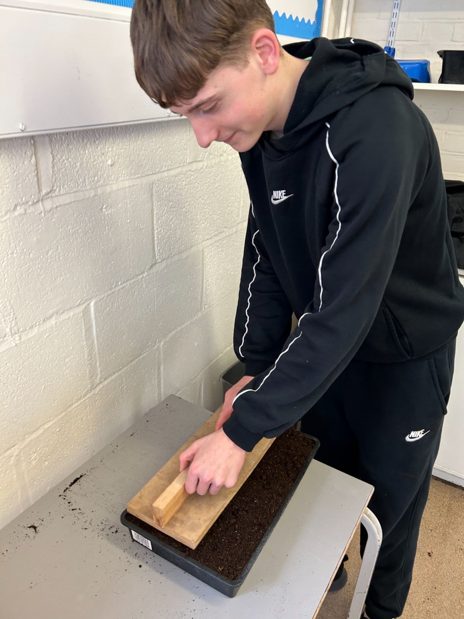 Student preparing a seed tray using a wooden tool