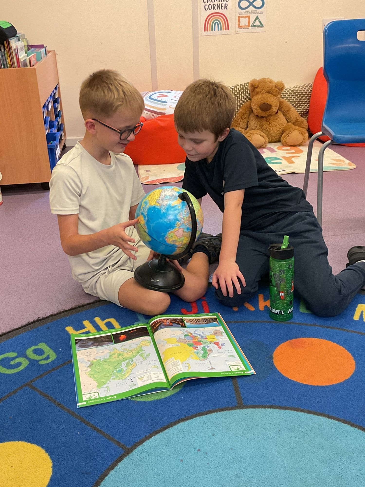 Two students sat on a carpet exploring a globe of the world