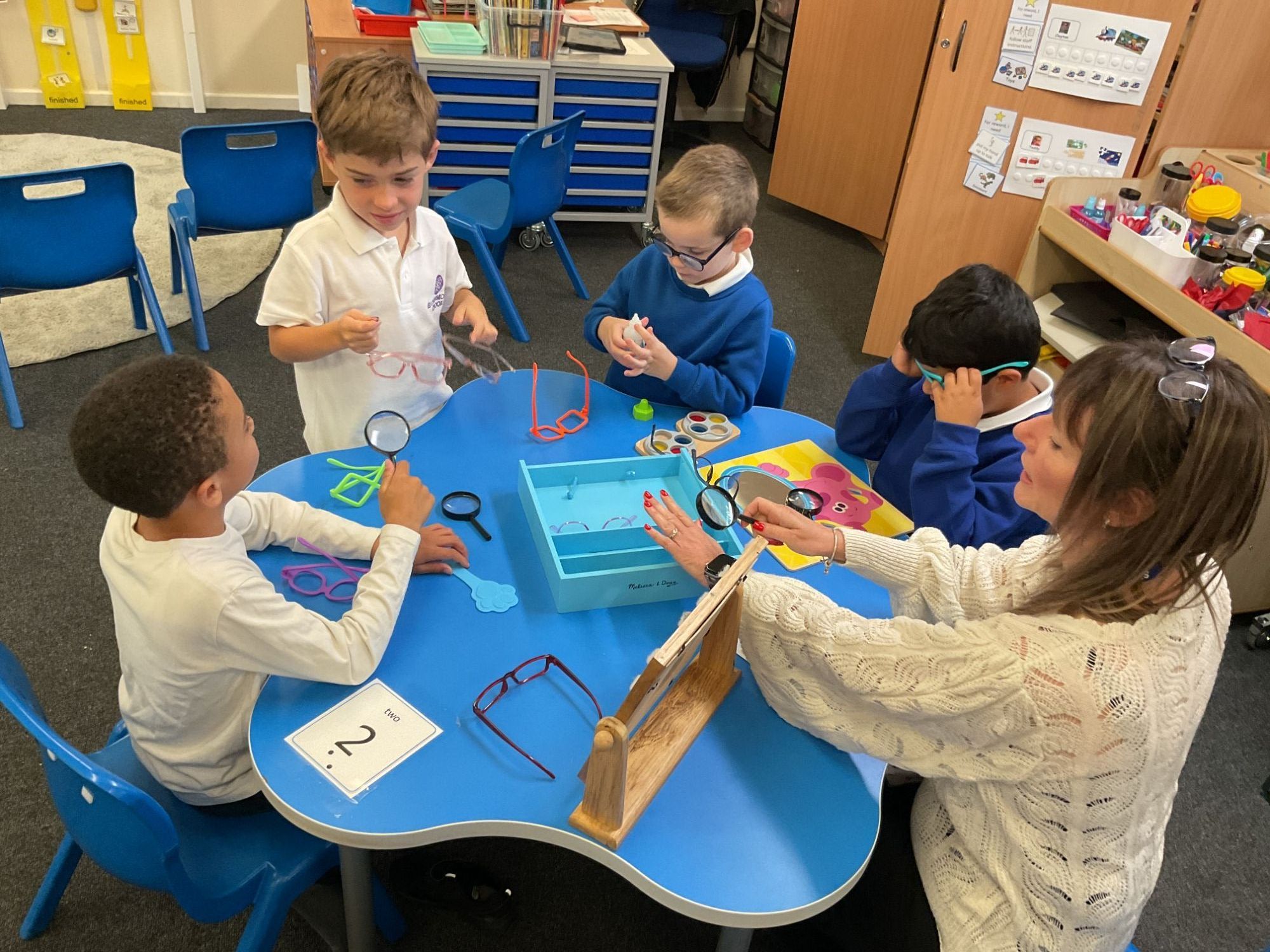 Four students sat round a table with their teacher using magnifying glasses