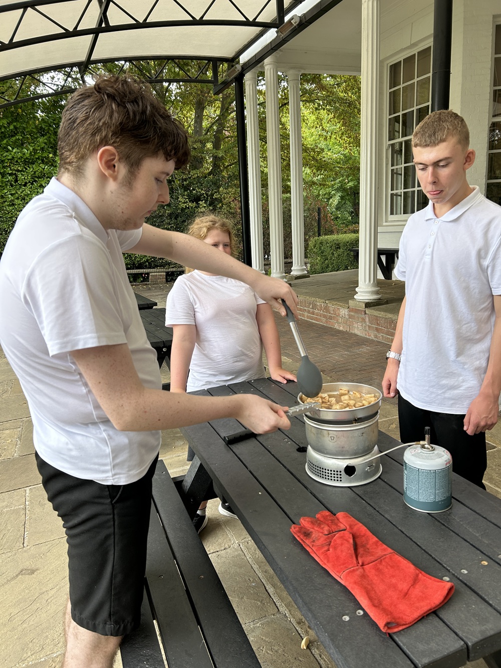 Three students outside cooking on a Trangia Stove