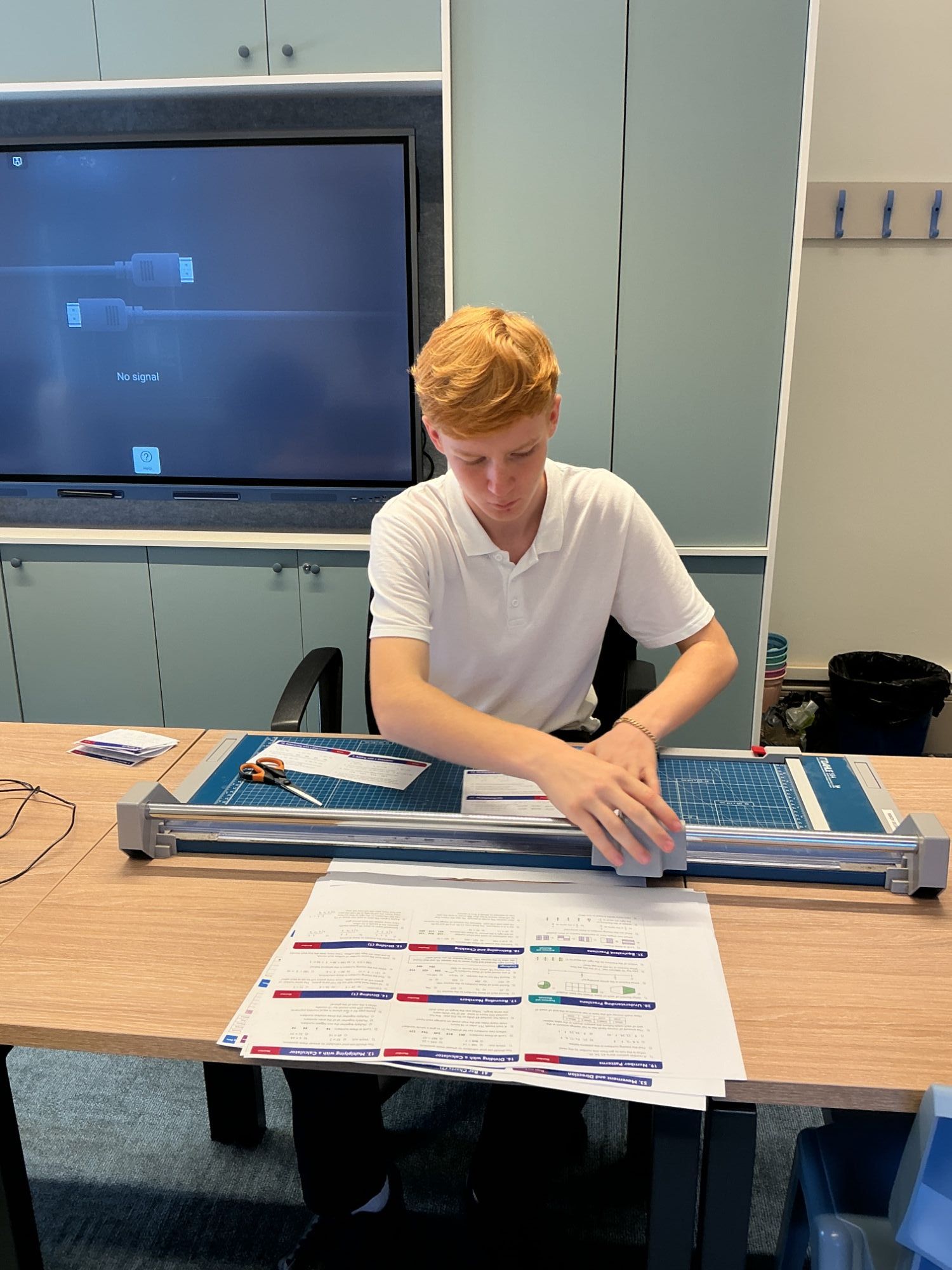 Student sat at a table carefully cutting with the school guillotine