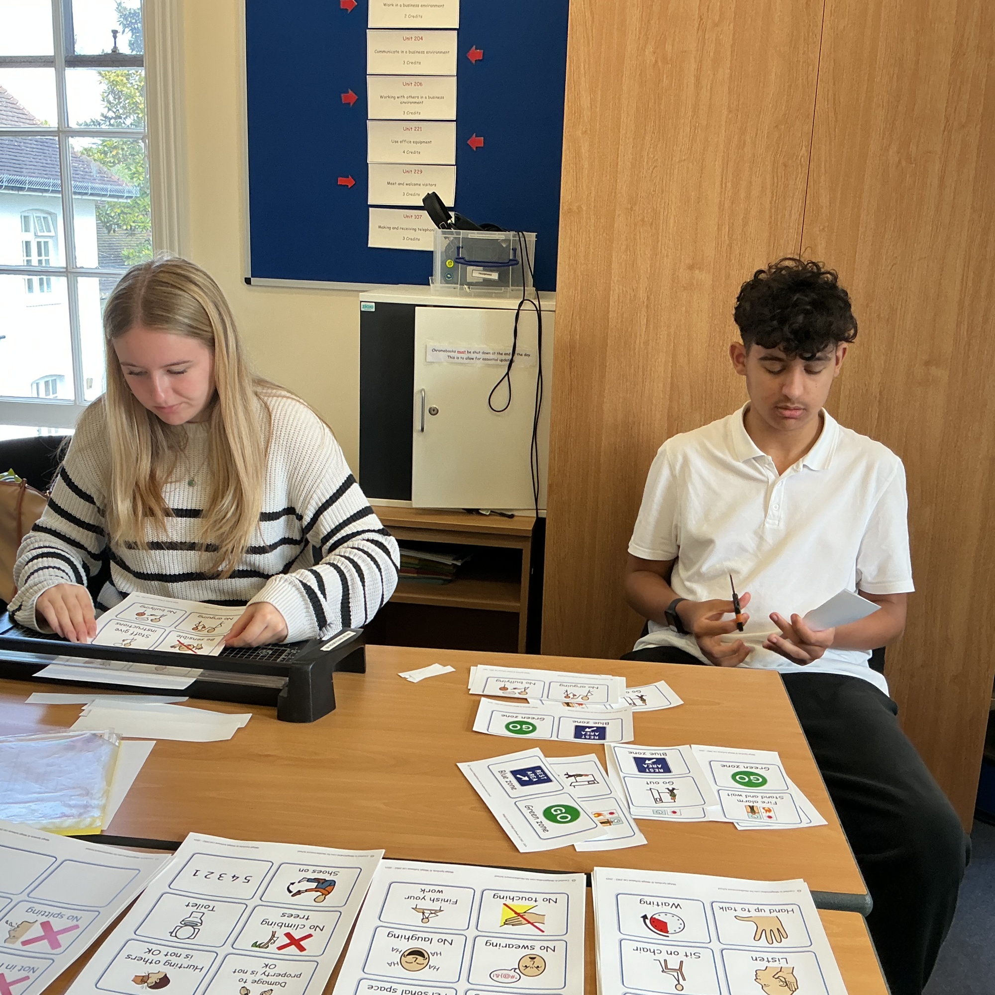 Business Admin students cutting out pictures with a guillotine for the packs