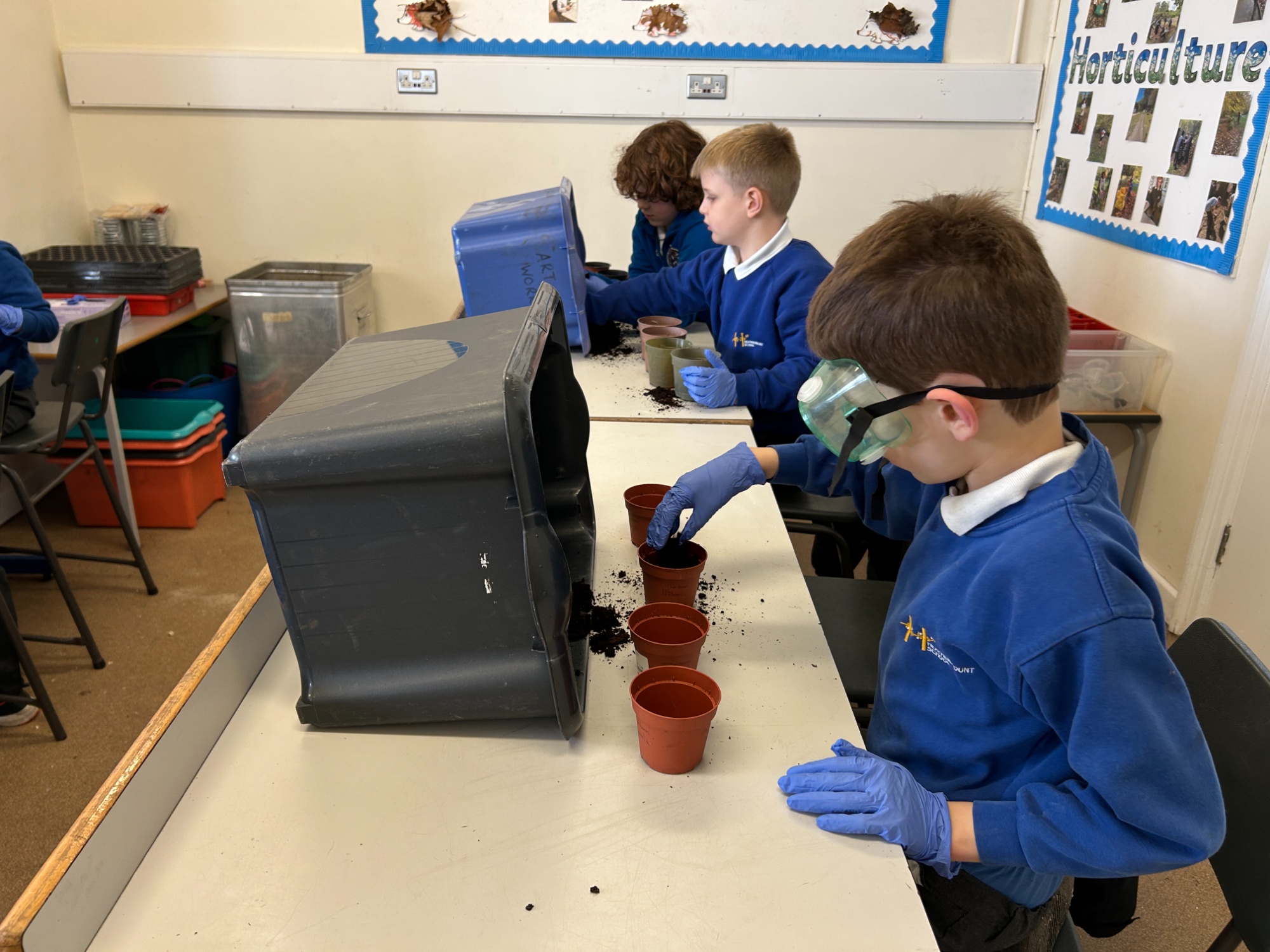 Boys carefully filling a line of plant pots with soil