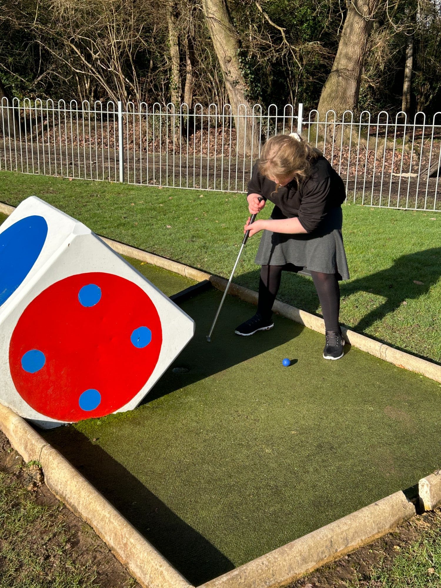 Girl lining up her golf shot at a hole with a big dice obstacle