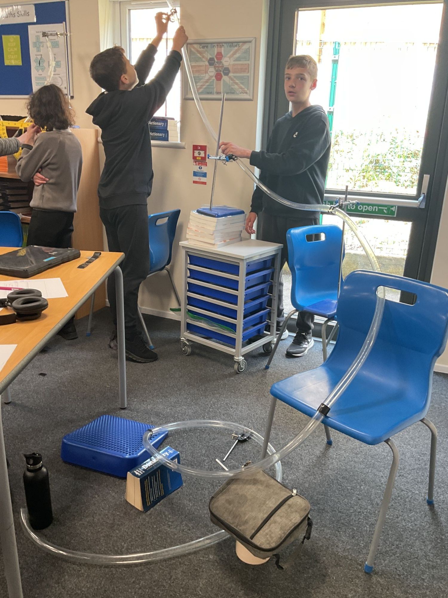 Three students setting up a tube across the classroom with lots of twirls for their roller coaster experiment