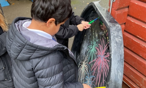 Two students from Apple Class drawing fireworks with coloured chalk