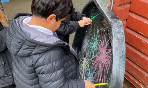 Two students from Apple Class drawing fireworks with coloured chalk