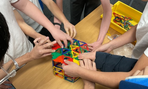 Student hands constructing a net to with brightly coloured plastic shapes to undestand surface area