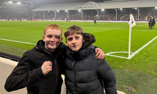 Two students with their arms round each other in front of the pitch