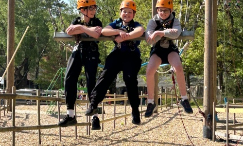 Three students wearing safety hemets raised up in the air on a wooden swing