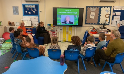 EYFS students sitting in a semi circle watching a presentation on the life of David Attenborough.