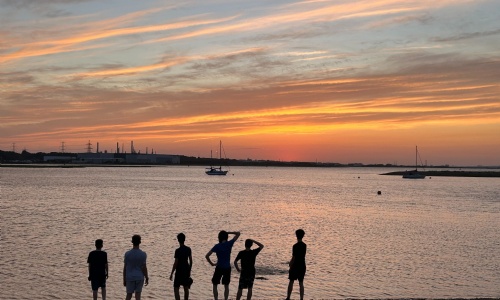 Students looking out over the water silhouetted against the sunset