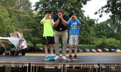 The headteacher with two students wearing their graduation hats and using their degree scrolls as telescopes