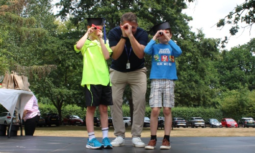 The headteacher with two students wearing their graduation hats and using their degree scrolls as telescopes