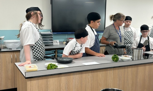 Catering teache explaining a recipe to a group of students at the front of the new classroom