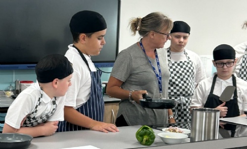 Catering teache explaining a recipe to a group of students at the front of the new classroom