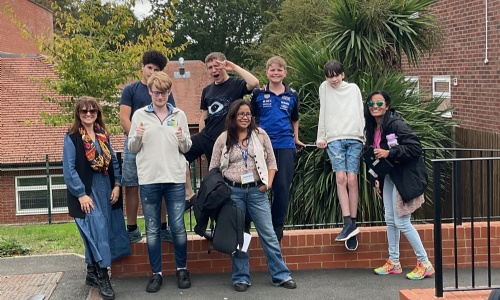 A small group of students and staff smiling wearing their jeans outside the modular building