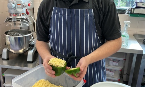 Student putting greated cheese on top of his stuffed pepper.