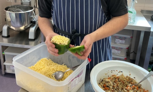 Student putting greated cheese on top of his stuffed pepper.
